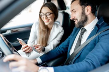 Businessman and woman dressed in the suits talking together while driving a luxury car in the city.