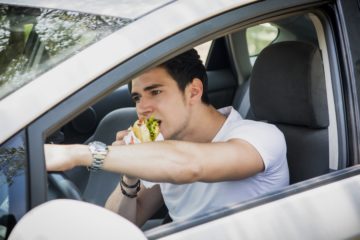 Young man is eating burger while driving.