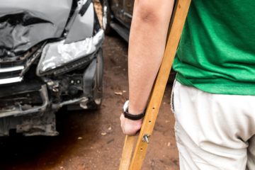 Injured driver with crutches looking at the damage car.